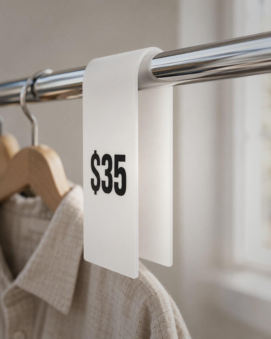 White acrylic rack sign showing a price, hanging on a clothes rail